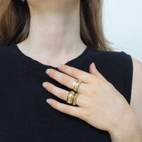 Woman wearing gold jewelry including earrings, rings, and a necklace on a plain background
