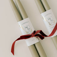 Two bundles of olive green taper candles with red ribbon.