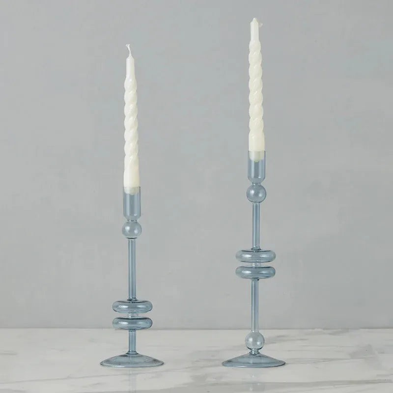 Two light blue glass candle holders with white candles on a gray background