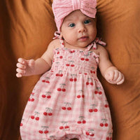 Baby wearing a pink romper with cherry pattern and matching headband on a brown background