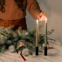 Person lighting two candles next to a holiday display.