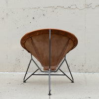 A mid-century modern spiral chair with a brown leather seat and backrest, supported by a black metal frame, photographed against a concrete wall.