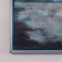 A close-up of a framed abstract painting featuring textured brushstrokes in shades of blue, gray, and black, mounted on a light pink wall.