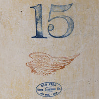 Vintage-style printed artwork or label showing the number 15 in blue at the top, a brown wing illustration in the middle, and a blue oval stamp reading Red Wing Cross Stencil Co. at the bottom on a textured beige background.