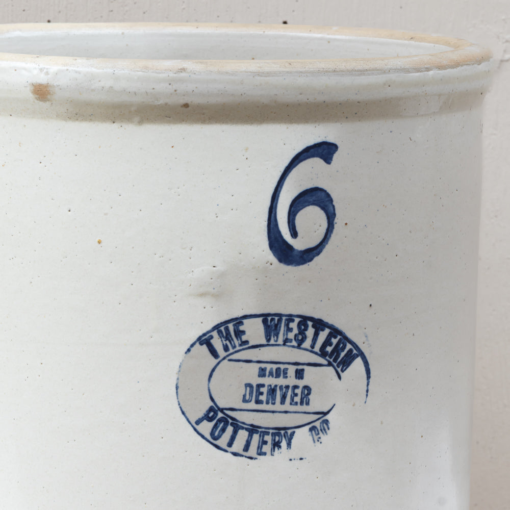 Close-up of a white speckled ceramic stoneware container with a blue printed number 6 and a circular stamp reading 'THE WESTERN POTTERY CO. MADE IN DENVER'.