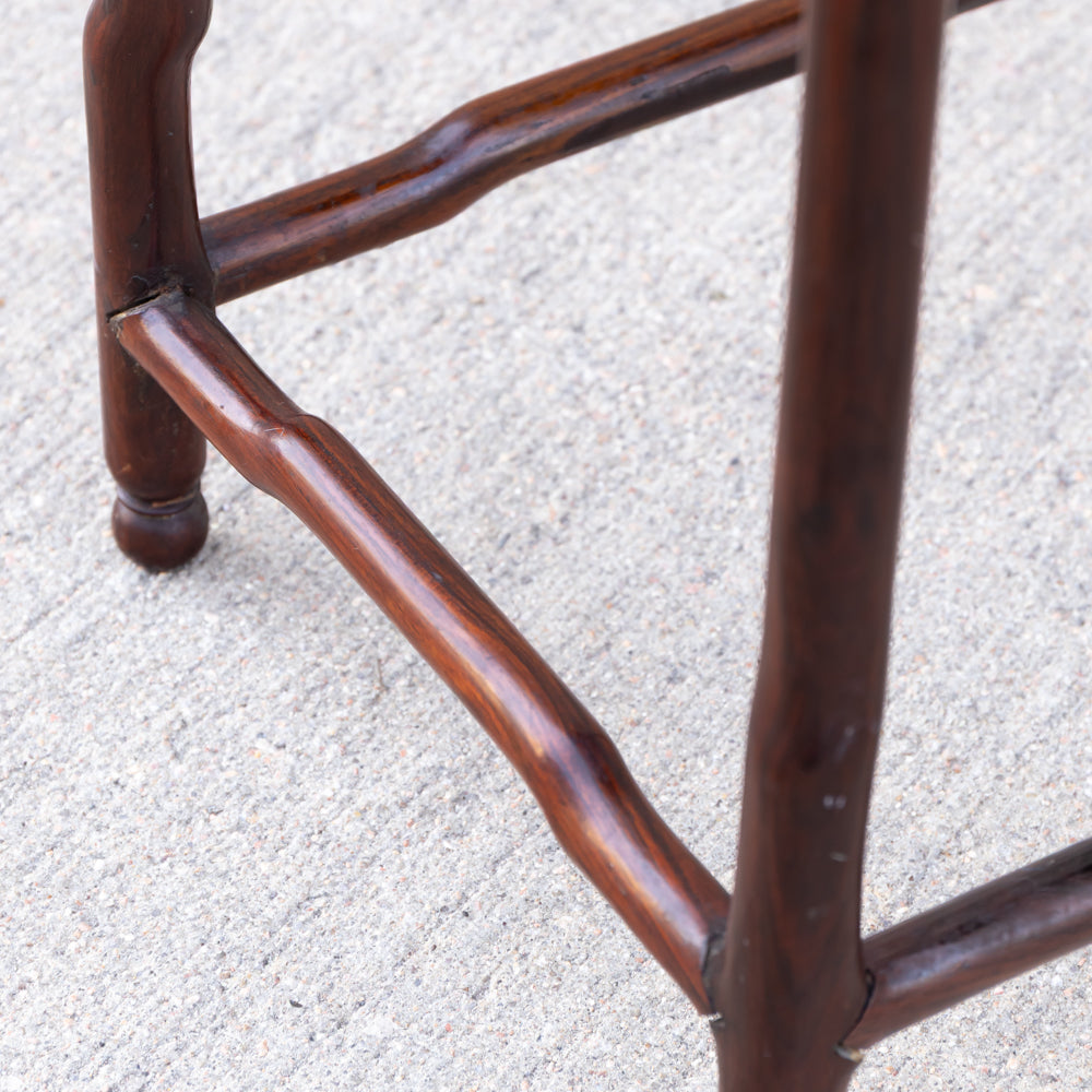 Close-up of a dark brown wooden stand or stool leg structure with curved joinery, photographed outdoors on a light gray concrete surface.
