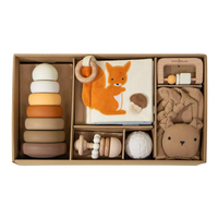 A coco village baby gift set in a brown cardboard box, featuring a wooden ring stack, a plush fox toy, a fabric teether, a wooden rattle, a textured ball, and a lion head cushion.