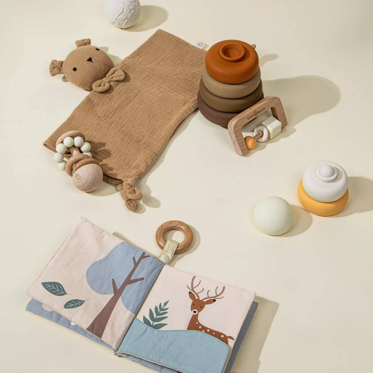 Collection of baby toys including a soft book, rattles, and a teething ring on a light background