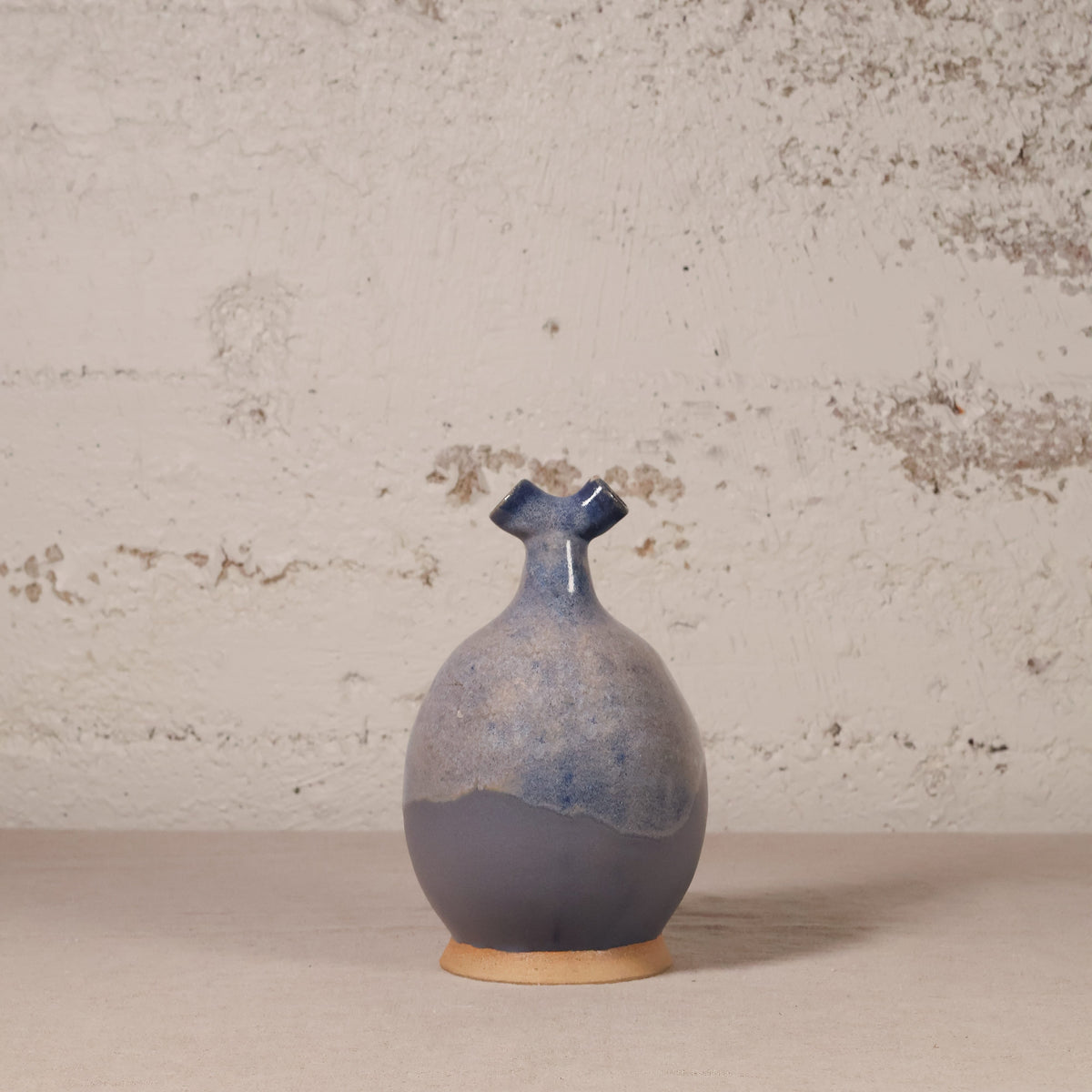 Blue ceramic vase on a beige surface with a textured wall background