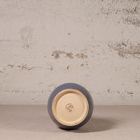 Ceramic vase with a blue exterior and beige interior on a textured surface.