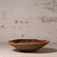 A rustic hand-carved wooden bowl with a natural organic pattern, displayed on a neutral surface against a textured plaster wall.
