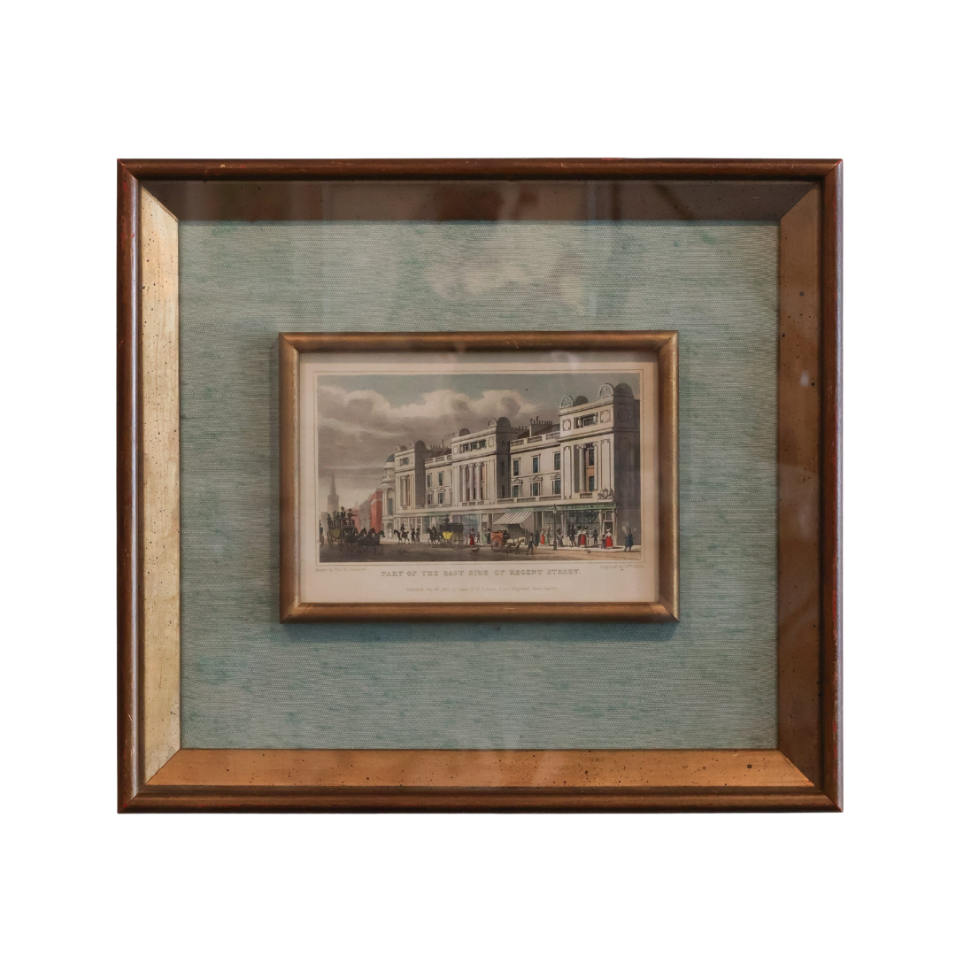 A framed vintage architectural print depicting a grand building facade, mounted on a textured blue-green mat within a dark brown wooden frame.