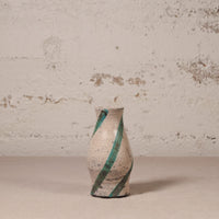 Ceramic vase with green stripes on a textured surface and wall background