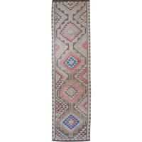 A long rectangular area rug with a geometric tribal pattern in pink, blue, gray, and beige on a white background.