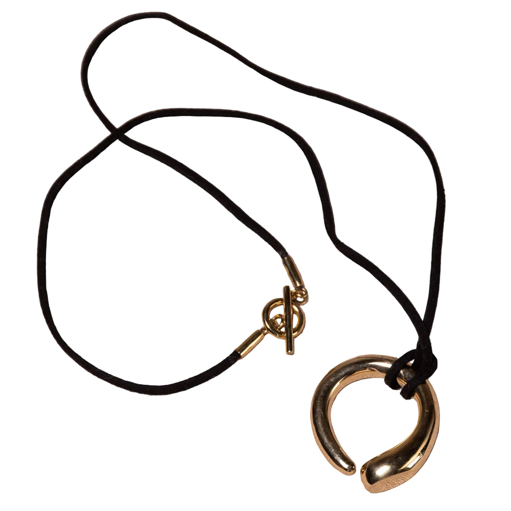 A black cord necklace with a polished gold-tone open hoop pendant and toggle clasp, displayed on a textured beige linen background.