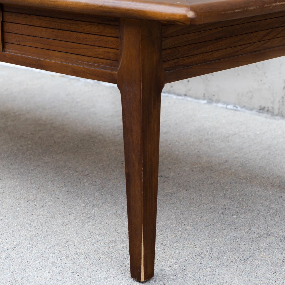 Close-up of a mid-century modern wooden table leg with a tapered design and a slatted drawer front, set on a gray concrete floor.