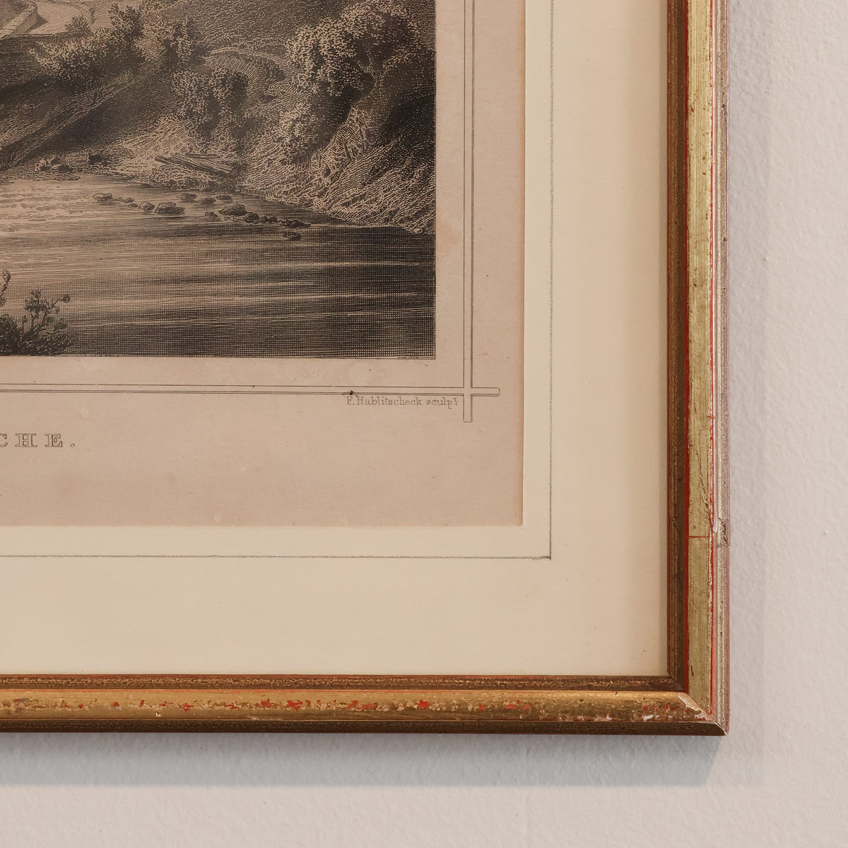 Framed vintage landscape print with a gold border on a textured wall.