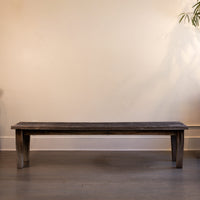 Wooden bench against a plain wall with a plant in the corner