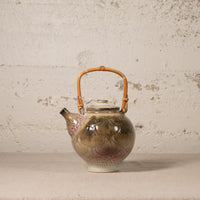 Ceramic teapot with a bamboo handle on a textured surface