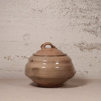 Brown ceramic jar with lid on a textured beige background
