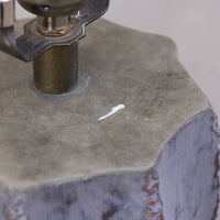 Close-up of a textured gray stone or concrete sample block with a cylindrical metal fixture pressing into it, showing a small white mark on the surface.
