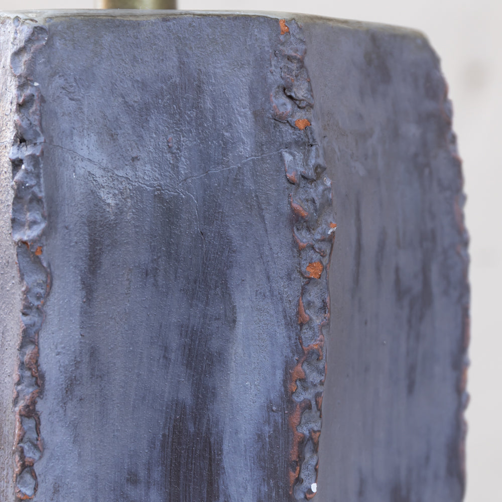 Close-up of a dark charcoal gray cast iron or steel block with textured, rough edges and a vertical seam showing rusted orange highlights.