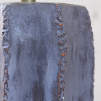 Close-up of a dark charcoal gray cast iron or steel block with textured, rough edges and a vertical seam showing rusted orange highlights.
