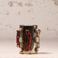 A vintage-style silver-toned cuff bracelet decorated with red enamel inlays, white pearl-like beads, and small silver studs, set against a textured off-white background.
