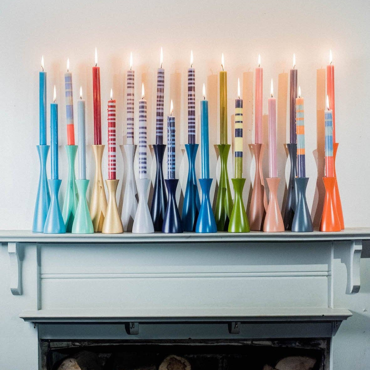 Colorful candles on a mantelpiece with logs below