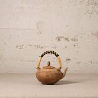 Brown ceramic teapot with a textured surface and wicker handle on a light gray background
