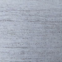 A close-up of a woven fabric texture in a light blue-gray color with subtle darker gray and brown flecks throughout.