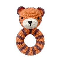 A crocheted tiger-themed baby teether with a ring handle, featuring orange and dark brown stripes, a cream-colored snout, and small black embroidered eyes and nose on a solid white background.