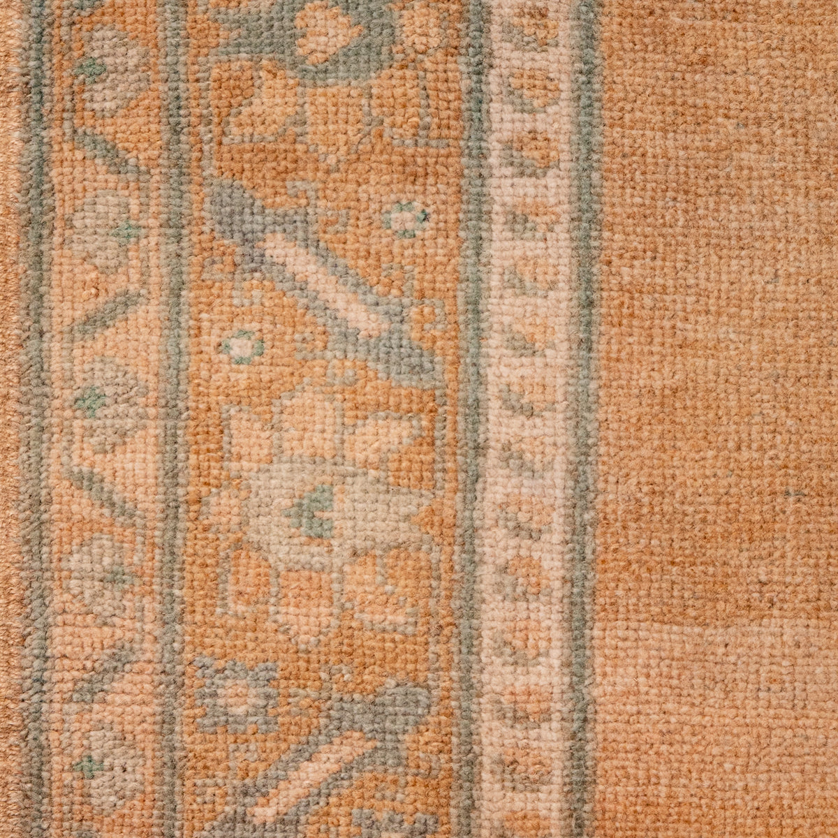 Close-up of a textured area rug with a warm orange base, featuring vertical bands of faded beige and muted sage green geometric patterns.