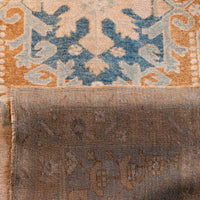Close-up of a patterned rug showing a warm orange and beige field with a blue geometric medallion above a heavily worn, faded brown lower section.