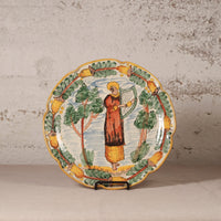 Decorative plate with a person playing a harp and surrounded by trees and birds on a textured wall background.