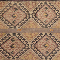 A close-up of a woven textile with a repeating geometric diamond pattern in beige, brown, muted red, and black, with a horizontal band of solid tan woven through the center.