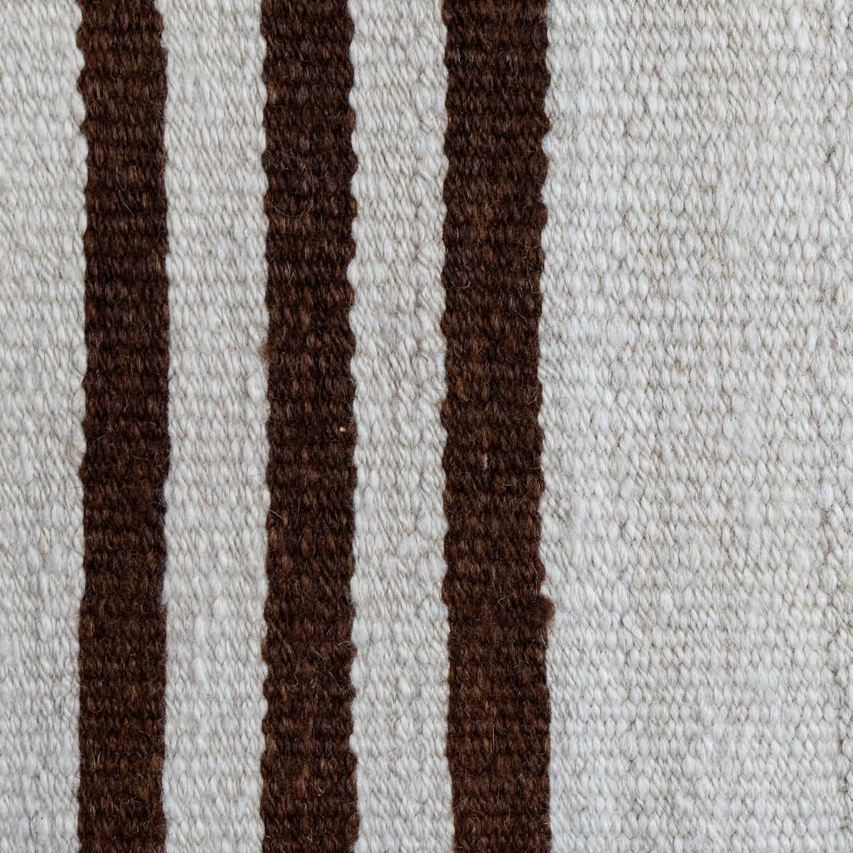 Close-up of a woven textile with vertical dark brown stripes on an off-white background.