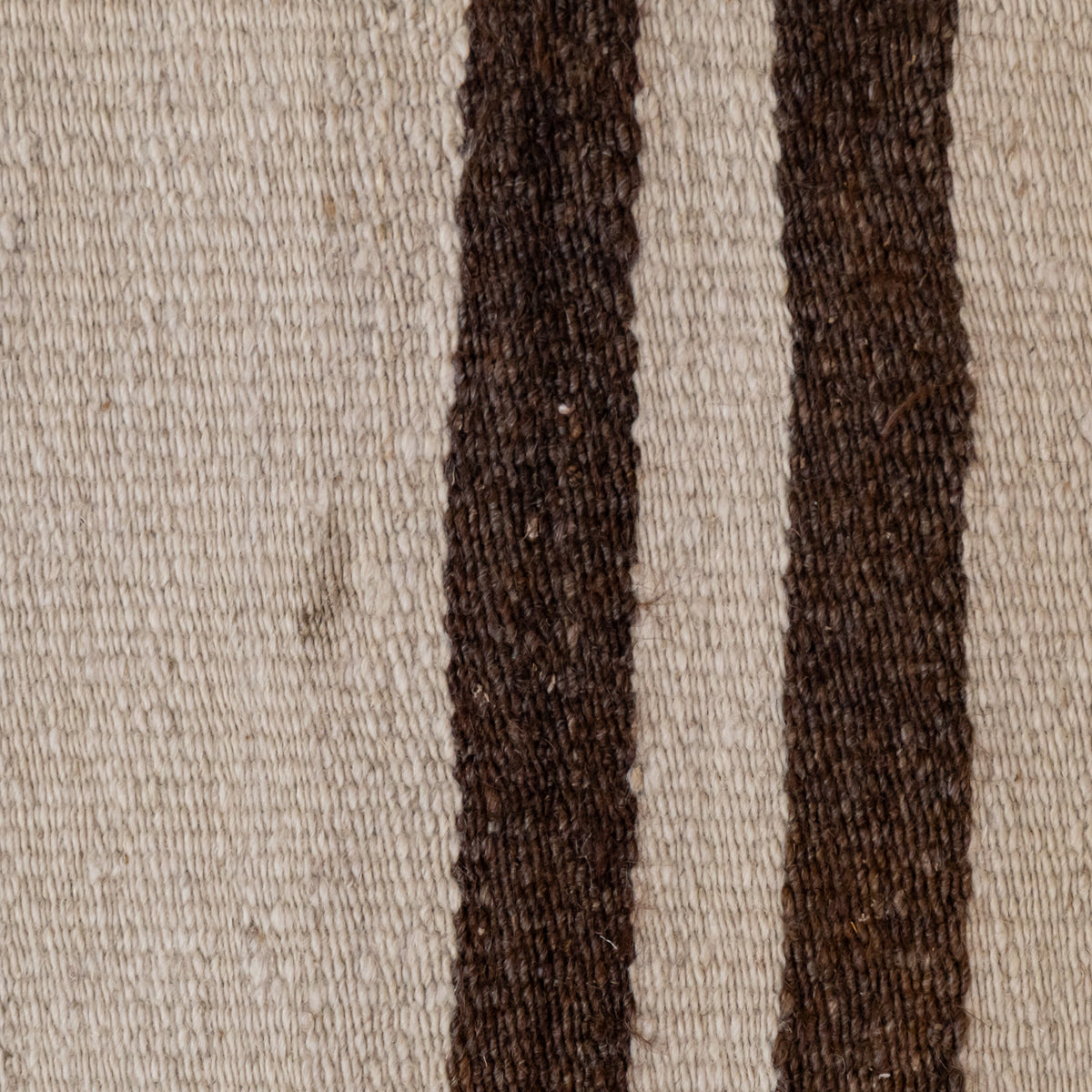 Close-up of a woven textile with a warm off-white background and two vertical dark brown stripes.