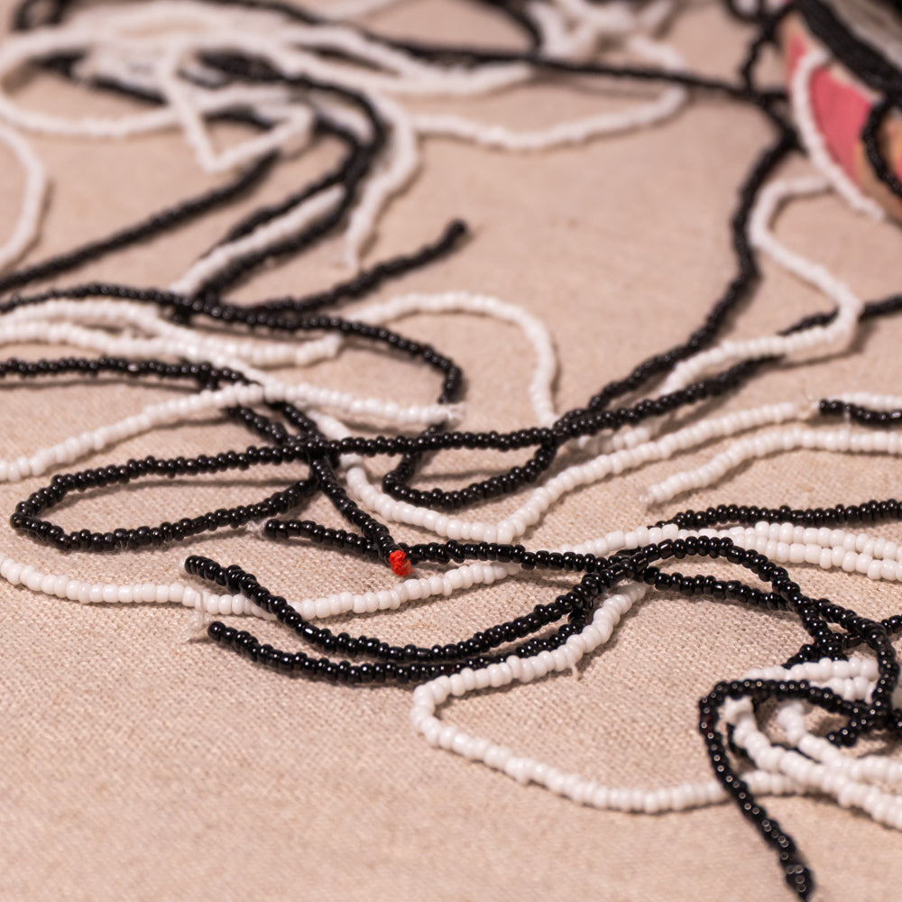 Close-up of loose black and white seed beads arranged on a beige fabric background, with a small red accent bead visible.