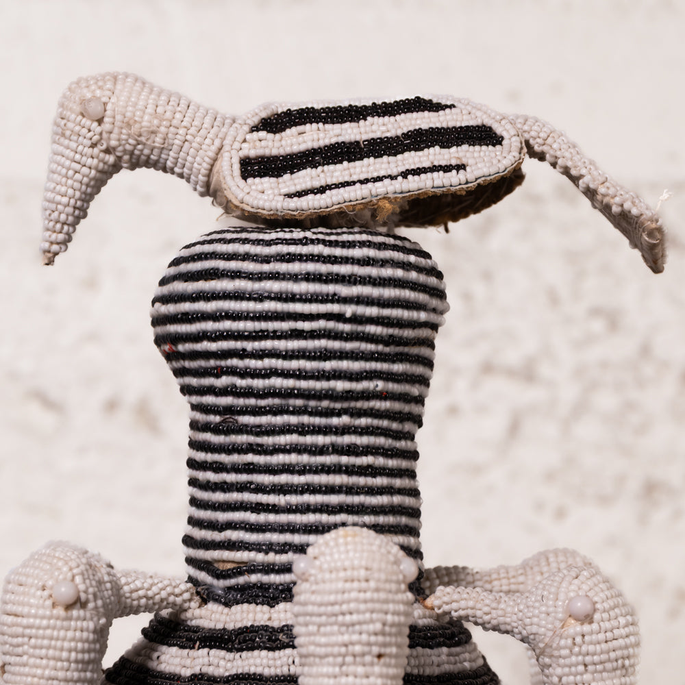 A handmade beaded doll with a striped black and white body and a striped head, photographed against a textured off-white background.