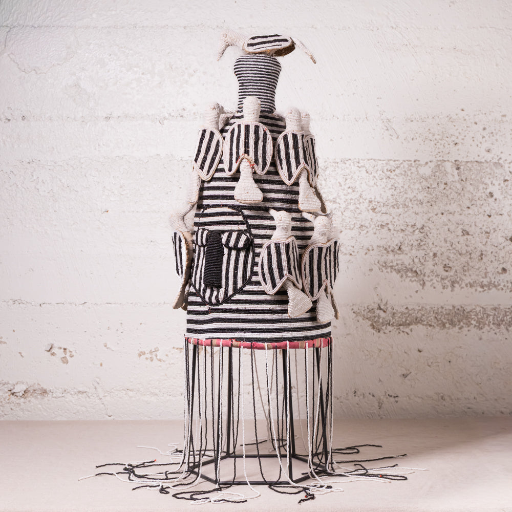 A handmade black and white striped textile sculpture or decorative art piece displayed on a wire frame against a textured white wall.