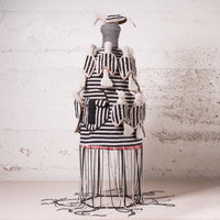 A handmade black and white striped textile sculpture or decorative art piece displayed on a wire frame against a textured white wall.