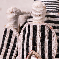 Close-up of hand-beaded African dolls, featuring black and white striped bodies made of small seed beads, with one doll in the foreground and another partially visible behind it.