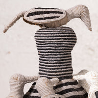 A handmade African beaded doll with a striped black and white body, a large striped head, and long pointed ears, shown against a neutral light background.