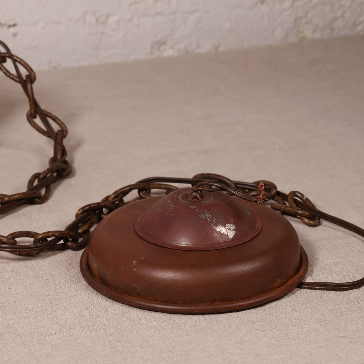 A vintage rusted metal ceiling light fixture canopy with a chain, shown on a neutral textured surface.
