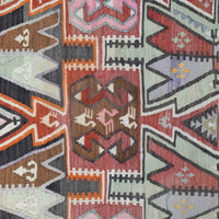 A close-up of a woven kilim textile with a geometric pattern in muted red, brown, gray, black, orange, and pale green.