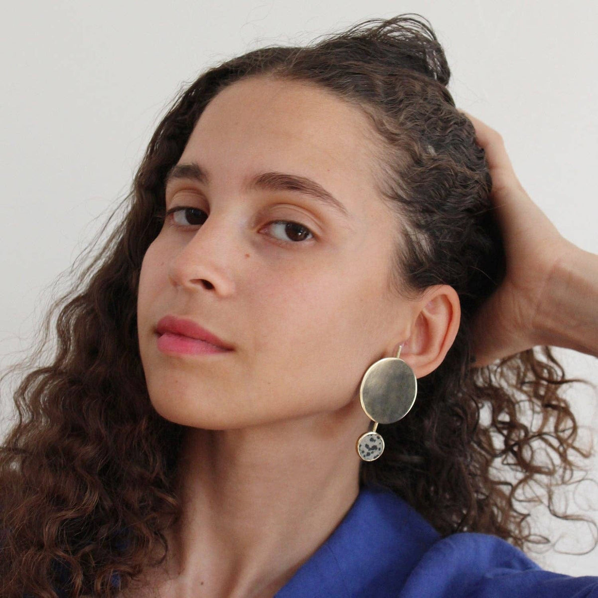 Woman with curly hair wearing a blue top and large earrings against a white background