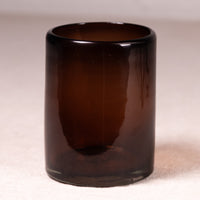 A dark amber brown translucent glass tumbler or candle holder, photographed against a neutral light beige background.