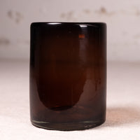 An empty dark amber brown glass tumbler or candle holder, photographed on a neutral light beige textured surface with a matching light background.