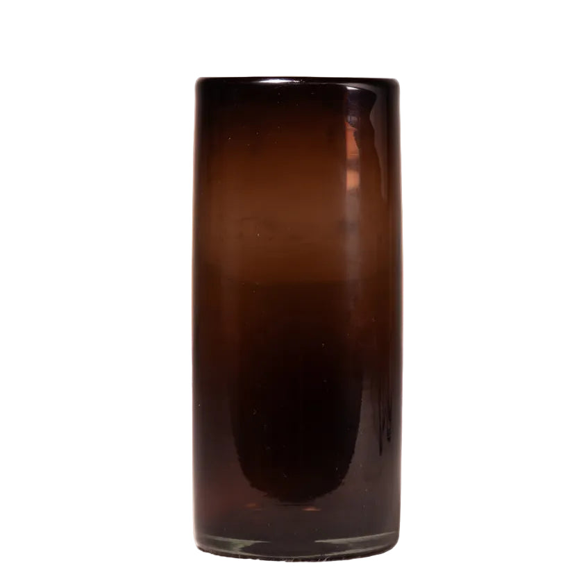 A tall, cylindrical dark amber-brown glass vase or candle holder with a smooth gradient from translucent amber at the top to deep brown at the bottom, set against a light textured off-white background.